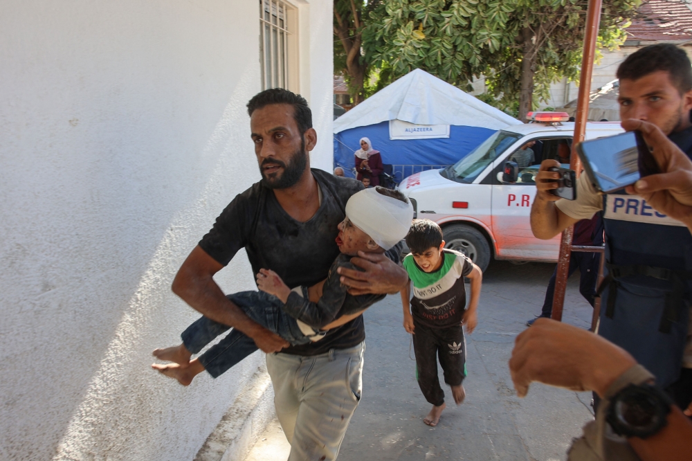 A Palestinian man rushes a child injured in Israeli military operations in northern Gaza, into Al-Ahli Arab hospital, also known as the Baptist hospital in Gaza City on October 21, 2024. (Photo by Omar Al-Qattaa / AFP)