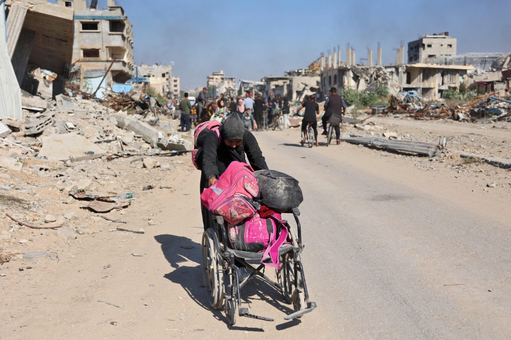 A woman pushing a wheel chair loaded with her personal belongings as displaced Palestinians fleeing Israeli military operations in Beit Lahia in the northern Gaza strip walk along the Salah al-Din main road in eastern Gaza City making their way to the city centre, on October 22, 2024. (Photo by Omar Al-Qattaa / AFP)