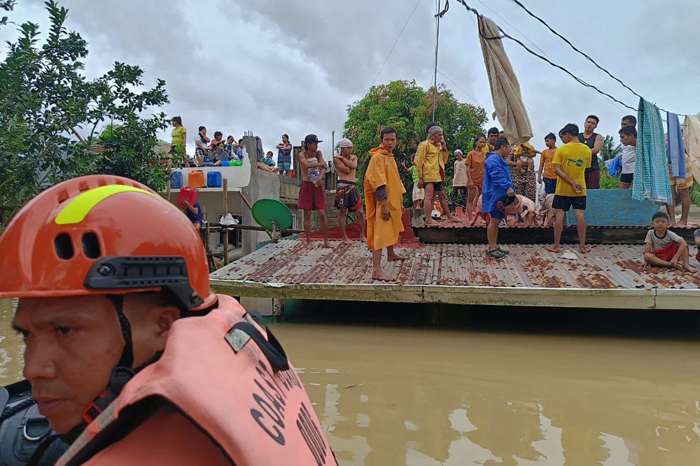 This handout photo taken and released on October 23, 2024 by the Philippine Coast Guard (PCG) shows residents affected by Tropical Storm Trami standing on the roofs of their submerged houses before being evacuated, in Libon town, Albay province, South of Manila. (Photo by Handout / Philippine Coast Guard (PCG) / AFP) 