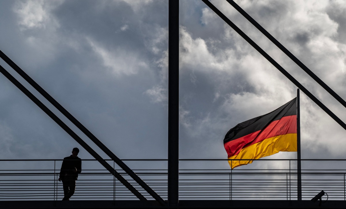 A man pauses on a pedestrian bridge as a German flag flies over the Reichstag building in Berlin on October 23, 2024. (Photo by John MACDOUGALL / AFP)
