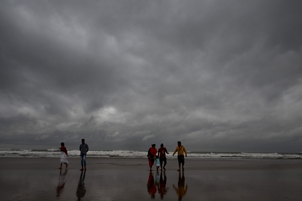 Dark clouds loom over the sea as local people and tourists walk along a beach in Digha, around 200km southwest of Kolkata, on October 24, 2024. (Photo by Dibyangshu SARKAR / AFP)