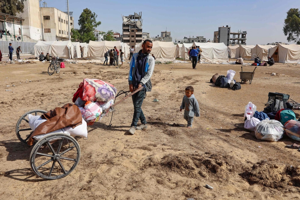 A displaced Palestinian man who fled Israeli army operations in the northern Gaza Strip, transports his belongings using a makeshift cart, in front of a newly set up tents at the Yarmouk Sports Stadium, once a football arena, in Gaza City on October 25, 2024. (Photo by Omar Al-Qattaa / AFP)
