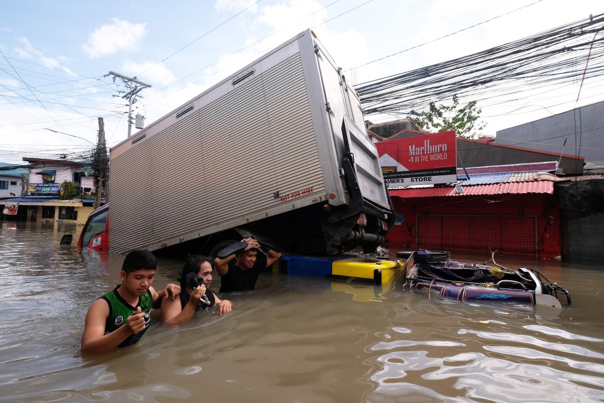 People wade through a flooded road brought about by Tropical Storm Trami, in Naga, Camarines Sur on October 25, 2024. (Photo by ZALRIAN SAYAT / AFP)