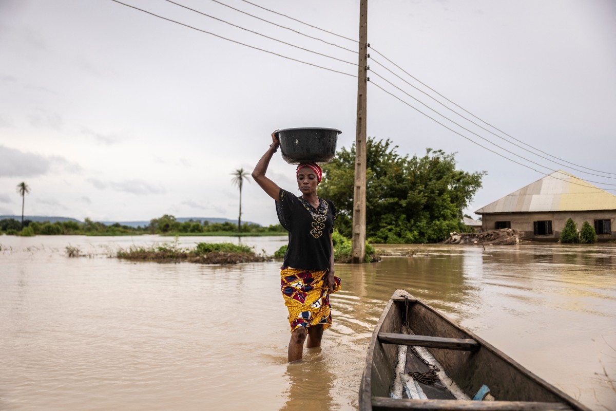 A woman balances a bucket on her head as she wades through a flooded area in Adaha, on October 22, 2024. Photo by OLYMPIA DE MAISMONT / AFP.