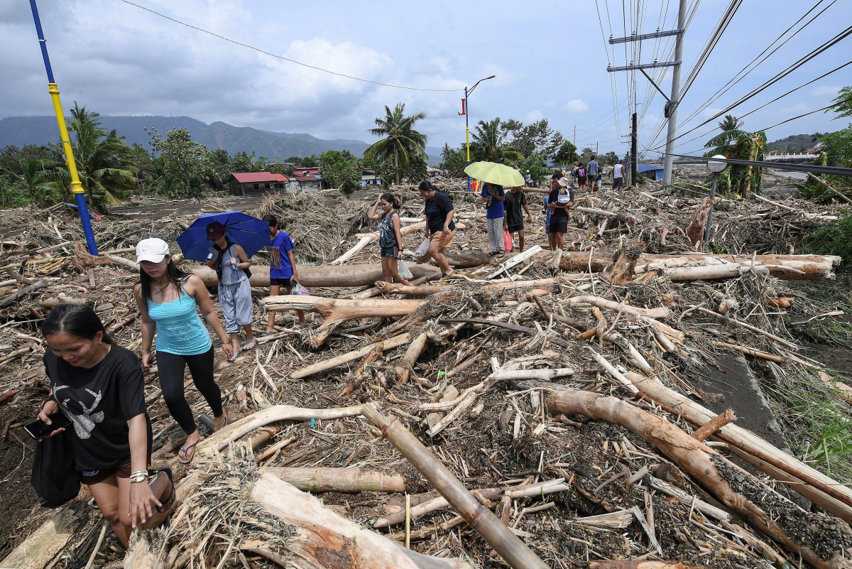 People walk amongst debris of logs swept away due to heavy rains brought about by Tropical Storm Trami in Laurel, Batangas province, south of Manila on October 25, 2024. Photo by Ted ALJIBE / AFP.