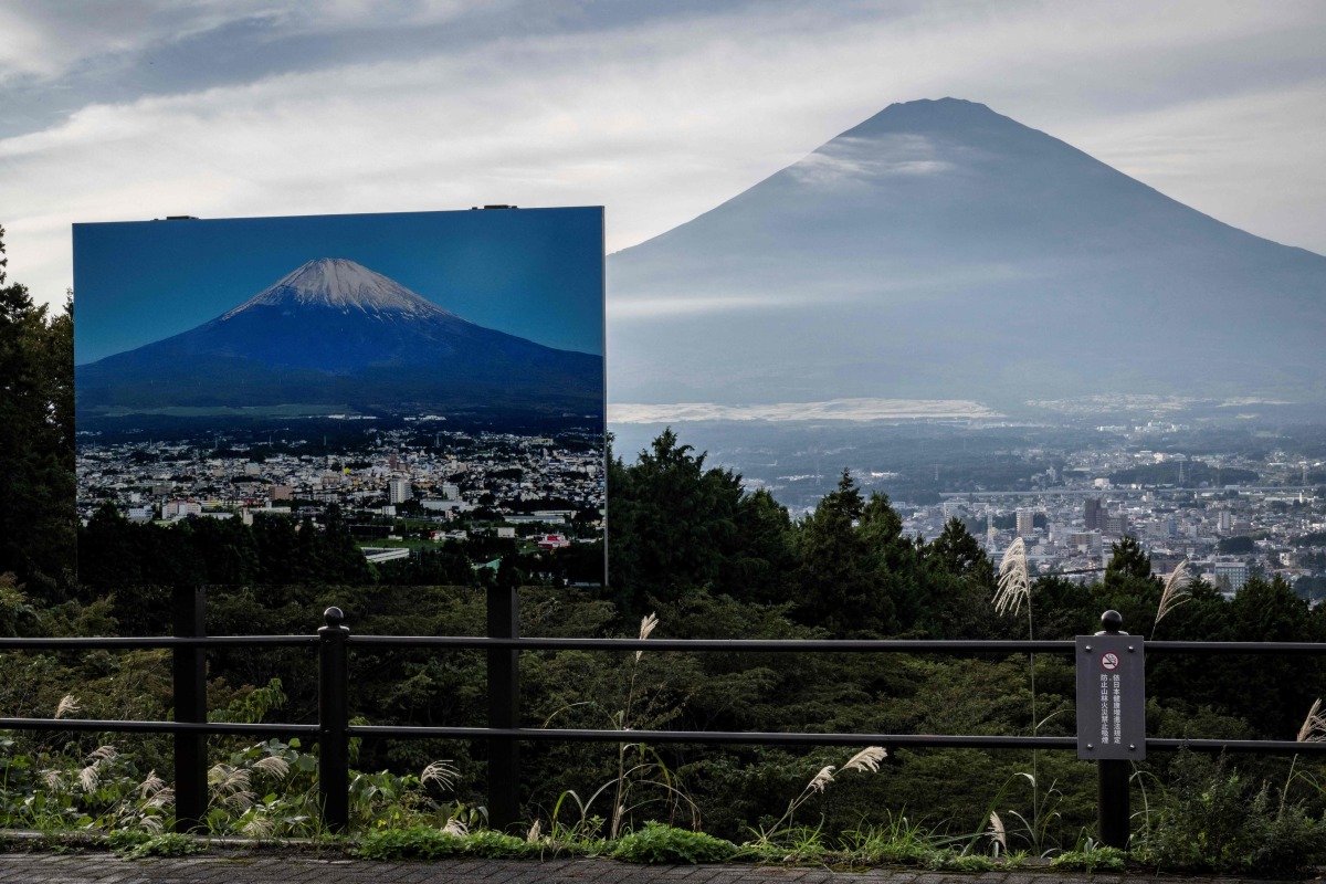 A sign with a photo of Mount Fuji covered in snow is seen at a view point as Mount Fuji, the highest mountain in Japan at 3,776 metres, looms in the background in Gotemba, Shizuoka prefecture on October 31, 2024. Photo by Yuichi YAMAZAKI / AFP