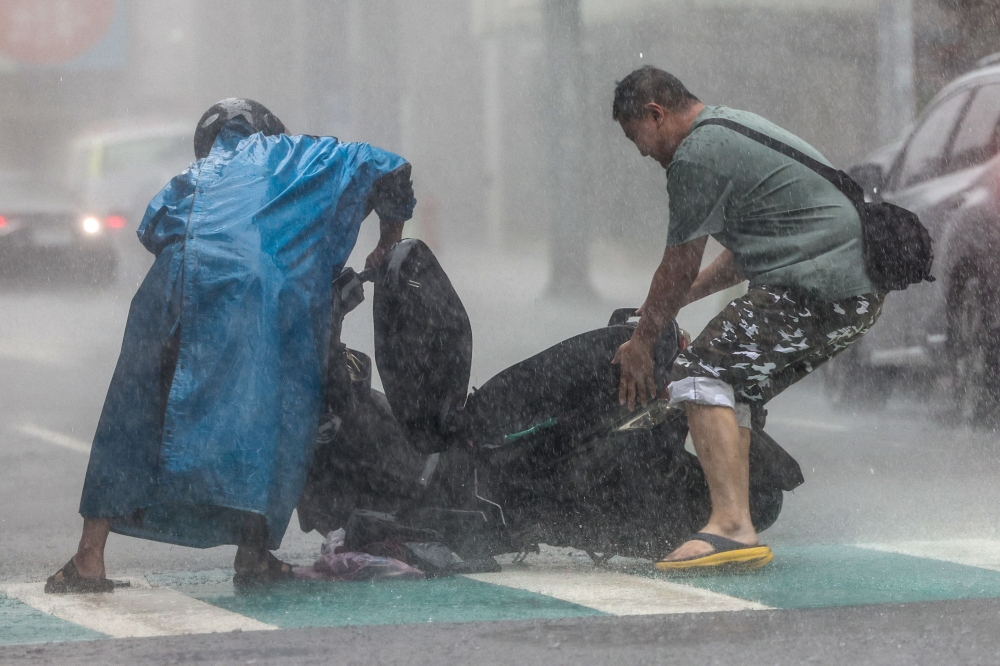 A man (R) helps a motorist with a scooter amid heavy rain due to Super Typhoon Kong-rey in Keelung on October 31, 2024. (Photo by I-Hwa Cheng / AFP)