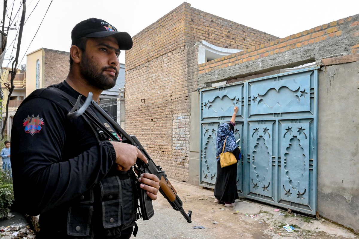 This photograph taken on October 29, 2024 shows an elite police personnel (L) standing guard as a health worker marks houses with numbers during a door-to-door poliovirus vaccination campaign for children on the outskirts of Peshawar. (Photo by Abdul MAJEED / AFP)
