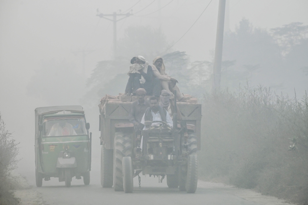 Commuters ride along a highway engulfed in smog, on the outskirts of Lahore on November 6, 2024. (Photo by Arif Ali / AFP)
