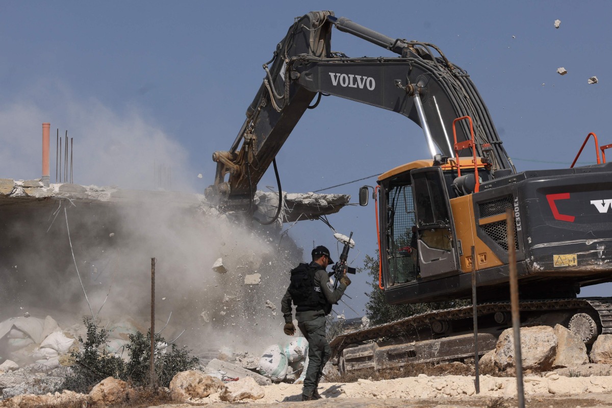 A member of the Israeli security forces walks past a bulldozer demolishing a house belonging to Palestinians, located in the area C, which lies under Israel's military control since 1967, in Yatta village in the southern area of the occupied West Bank, on November 6, 2024. (Photo by HAZEM BADER / AFP)
