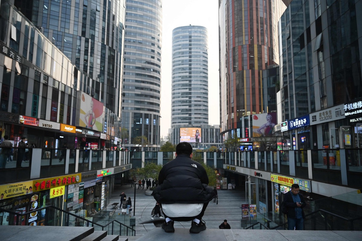 A man squats in a shopping mall in Beijing on November 8, 2024. (Photo by GREG BAKER / AFP)