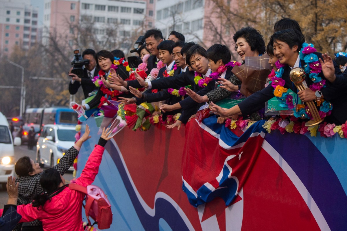 People (lower L) welcome members of the North Korean women's under-17 football team (R) on a street in Pyongyang on November 9, 2024. North Korea beat Spain on penalties November 3 in the Dominican Republic to clinch a record third Women's World Cup at under-17 level, adding it to their title in the under-20 version in September. (Photo by KIM Won Jin / AFP)
