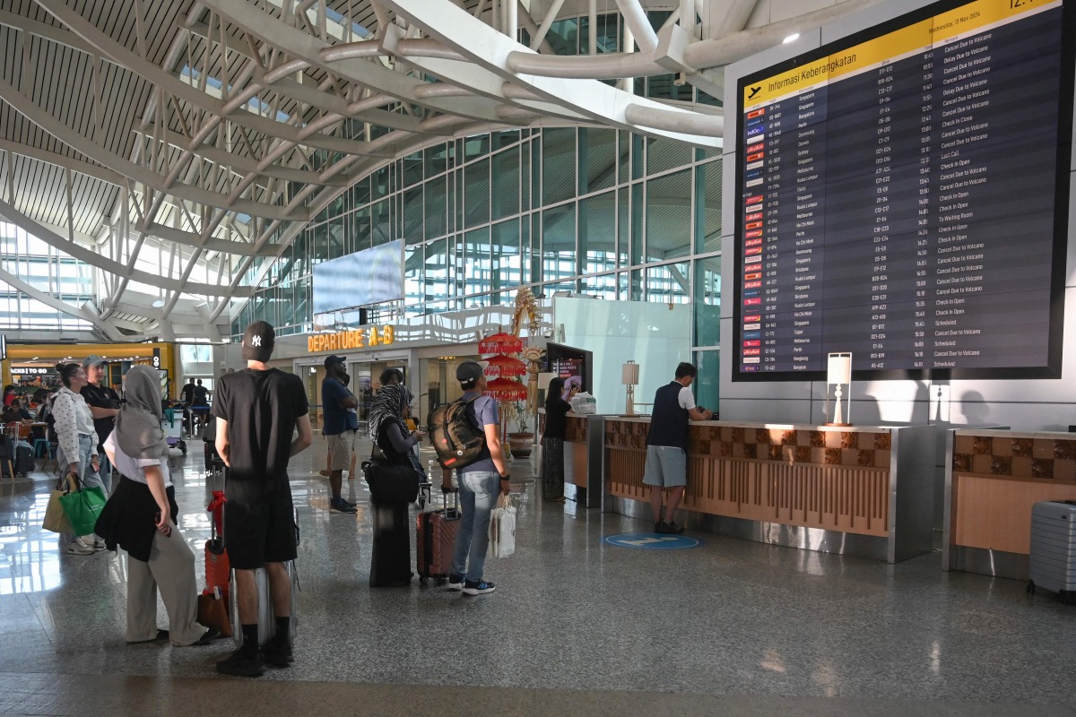 Passengers look at an electronic board displaying cancelled flights after the nearby Mount Lewotobi Laki-Laki volcano catapulted an ash tower miles into the sky, at the Ngurah Rai International Airport in Tuban near Denpasar, on Indonesia's resort island of Bali on November 13, 2024. (Photo by SONNY TUMBELAKA / AFP)