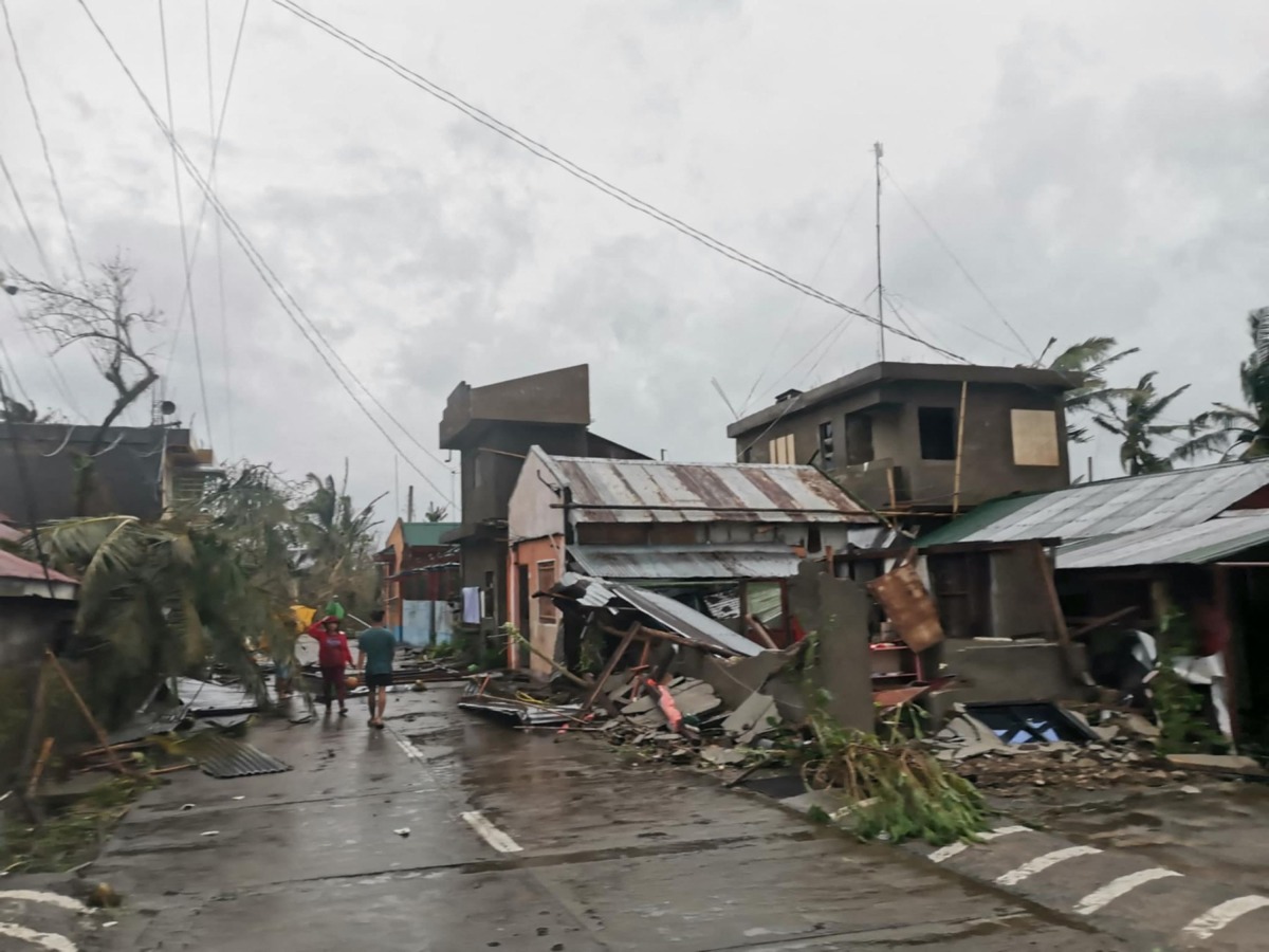 This handout photo released on November 17, 2024 through the courtesy of John Marshal Aquino Facebook page shows residents walking past destroyed houses in Panganiban town, Catanduanes province, after Super Typhoon Man-yi hit the province. Super Typhoon Man-yi uprooted trees, brought down power lines and ripped off corrugated iron roofing as it swept across the storm-weary Philippines on November 17, following an unusual streak of violent weather. (Photo by John Marshal Aquino / John Marshal Aquino / AFP)