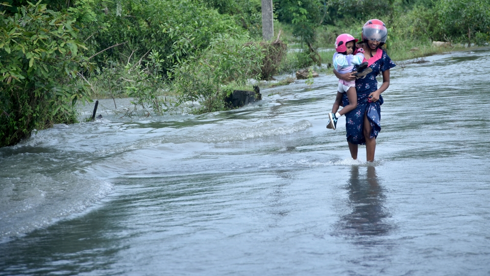 A woman holding a child in her arm wades through floodwater on a waterlogged road in Gampaha, Sri Lanka, on November 20, 2024. (Photo by Gayan Sameera/Xinhua)