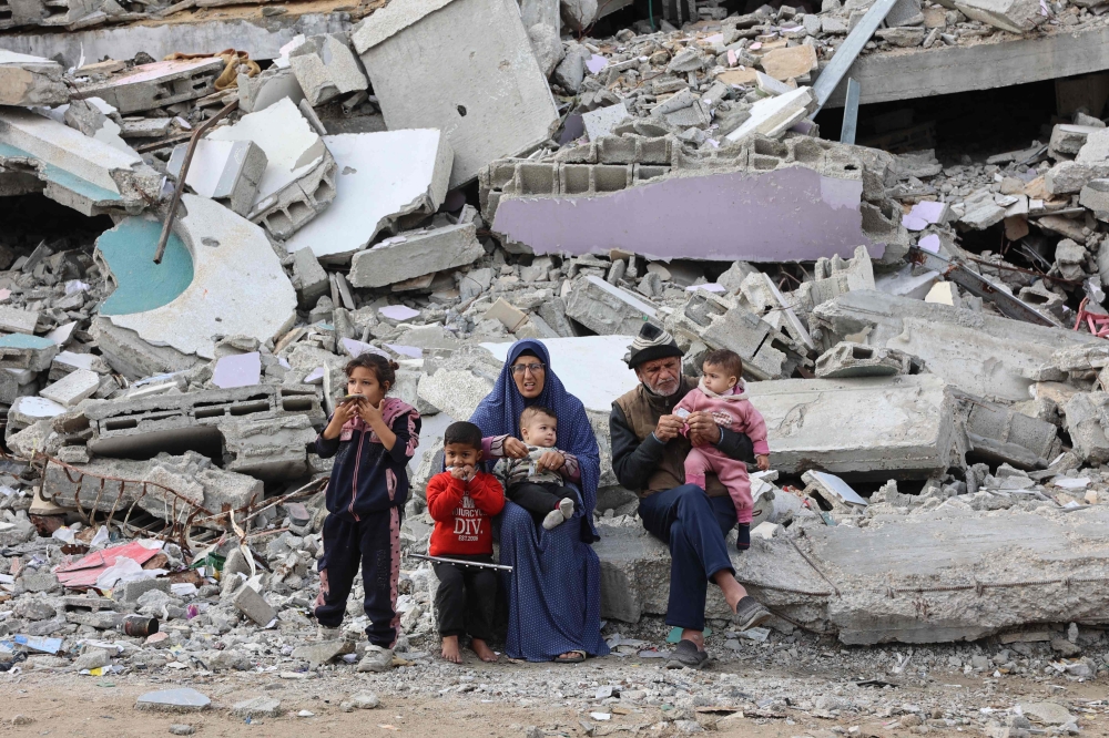 A Palestinian family rests on the rubble of a building west of Gaza City, on November 25, 2024. (Photo by Omar Al-Qattaa / AFP)