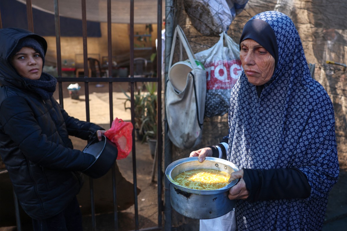 A displaced Palestinian woman carries food in container at a distribution centre in Deir el-Balah in the central Gaza Strip on November 26, 2024. Photo by BASHAR TALEB / AFP.