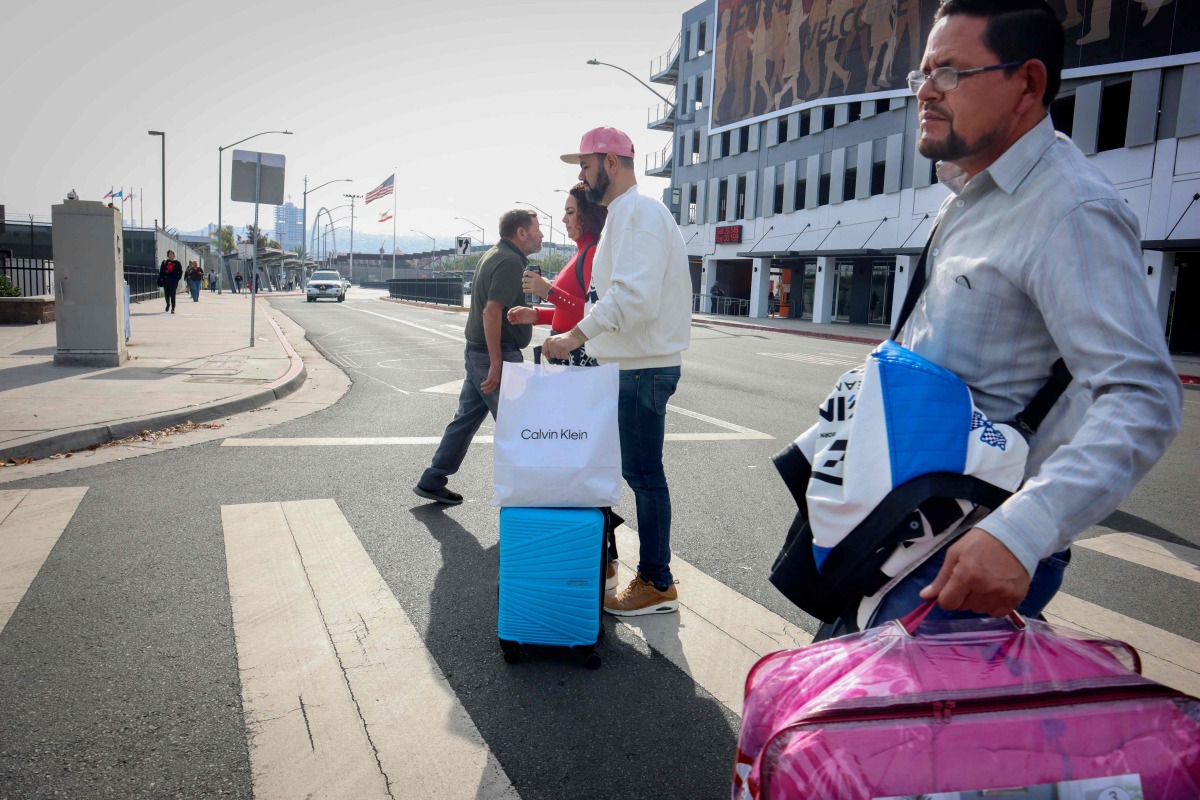 Shoppers walk across the street with their purchases near the US-Mexico border in San Ysidro, California, on November 26, 2024. (Photo by Sandy Huffaker / AFP)
