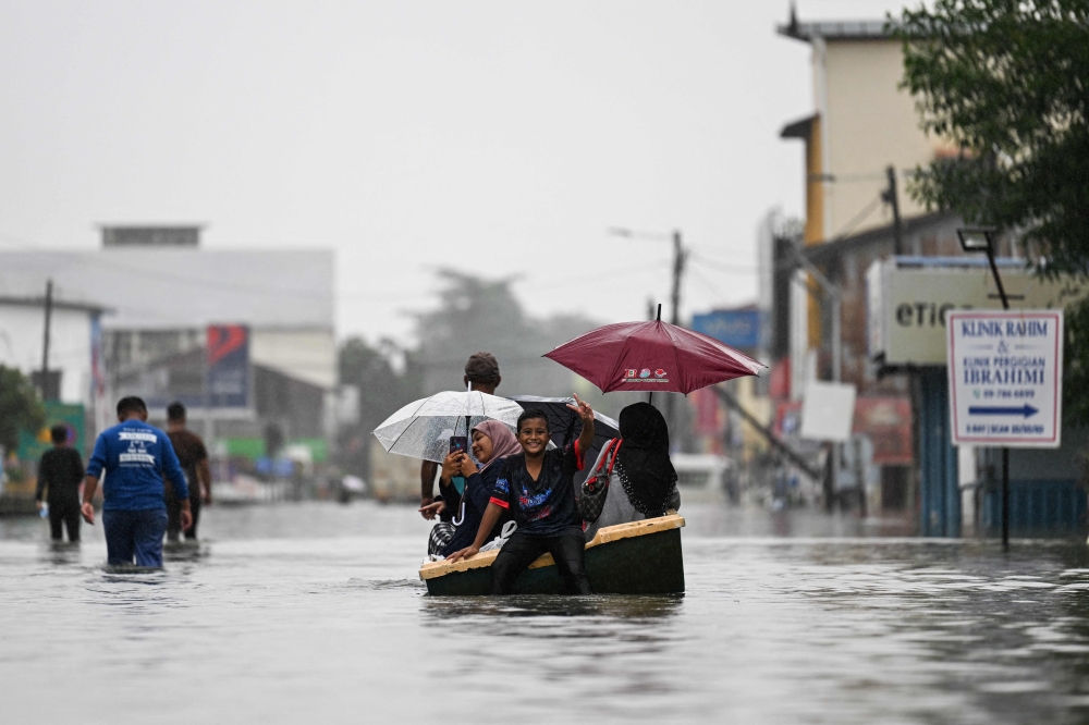 People use a boat through a flooded street during heavy rain in Pasir Puteh, in Malaysia's Kelantan state on November 30, 2024. (Photo by Mohd Rasfan / AFP)