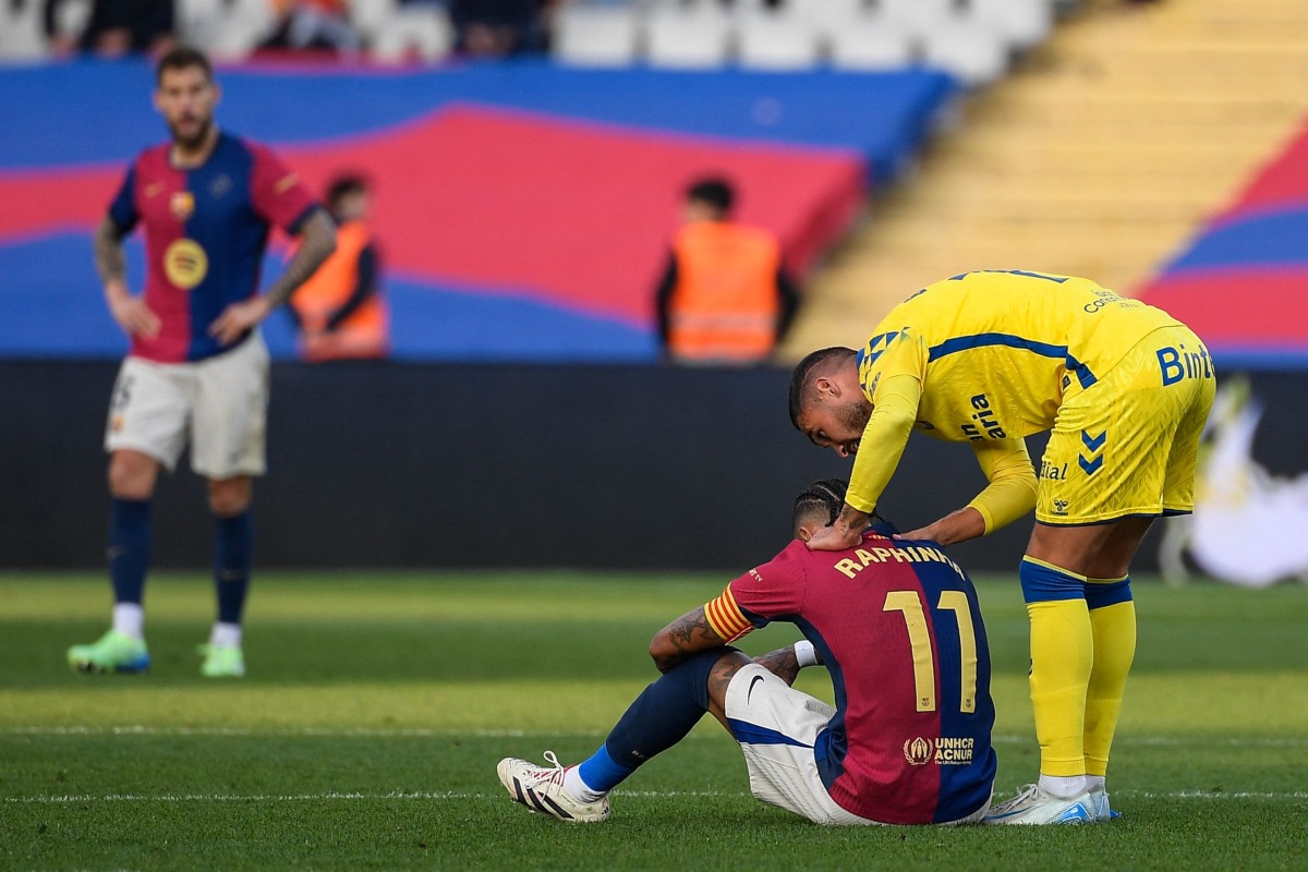 Barcelona's Brazilian forward #11 Raphinha (C) is consoled by Las Palmas' Spanish midfielder #11 Benito Ramirez (R) after their Spanish league football match between FC Barcelona and UD Las Palmas at the Estadi Olimpic Lluis Companys in Barcelona on November 30, 2024. (Photo by Josep LAGO / AFP)
