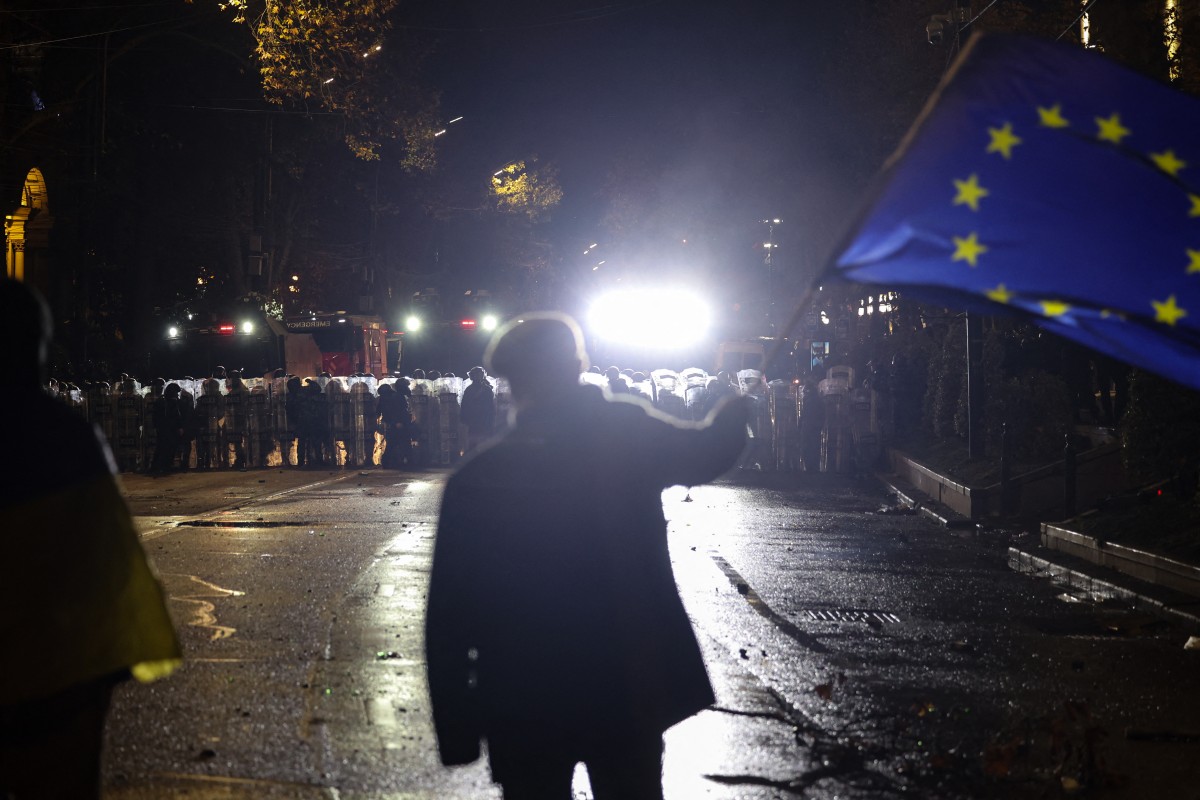 A protester waves a European Union flag in front of police during the fifth straight night of demonstrations against the government's postponement of EU accession talks until 2028, in central Tbilisi early on December 3, 2024. Photo by Giorgi ARJEVANIDZE / AFP.