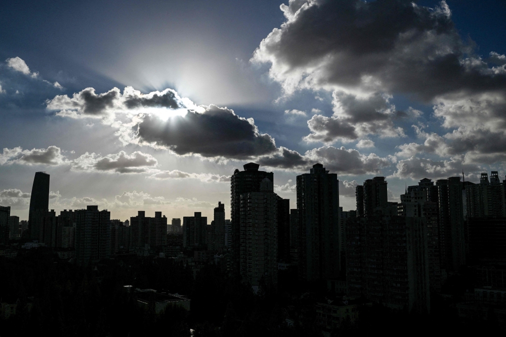 (Files) This file photo taken on September 17, 2024 shows buildings silhouetted as clouds drift past the sun in Shanghai. (Photo by Hector Retamal / AFP)