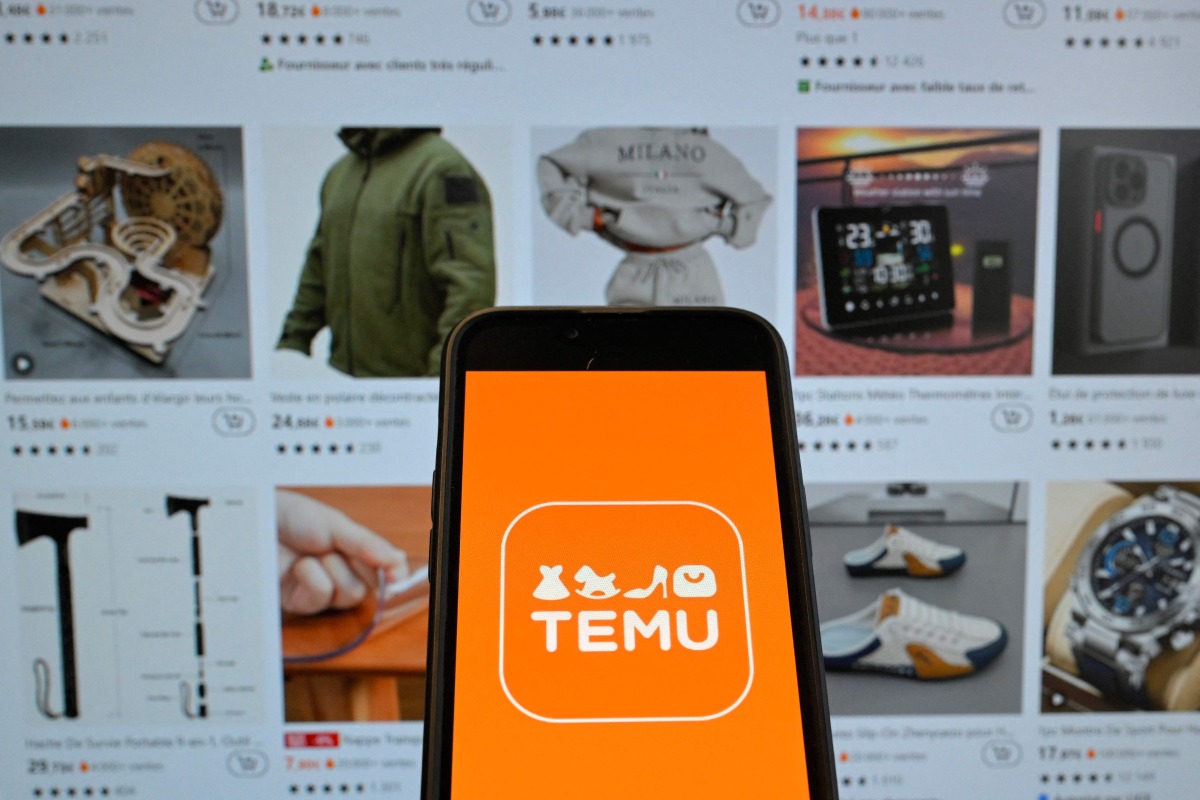 (FILES) This photograph shows the logo of Chinese e-commerce company Temu displayed on a mobile phone in front of a screen showing the company's website in Brussels on November 4, 2024. (Photo by Nicolas TUCAT / AFP)
