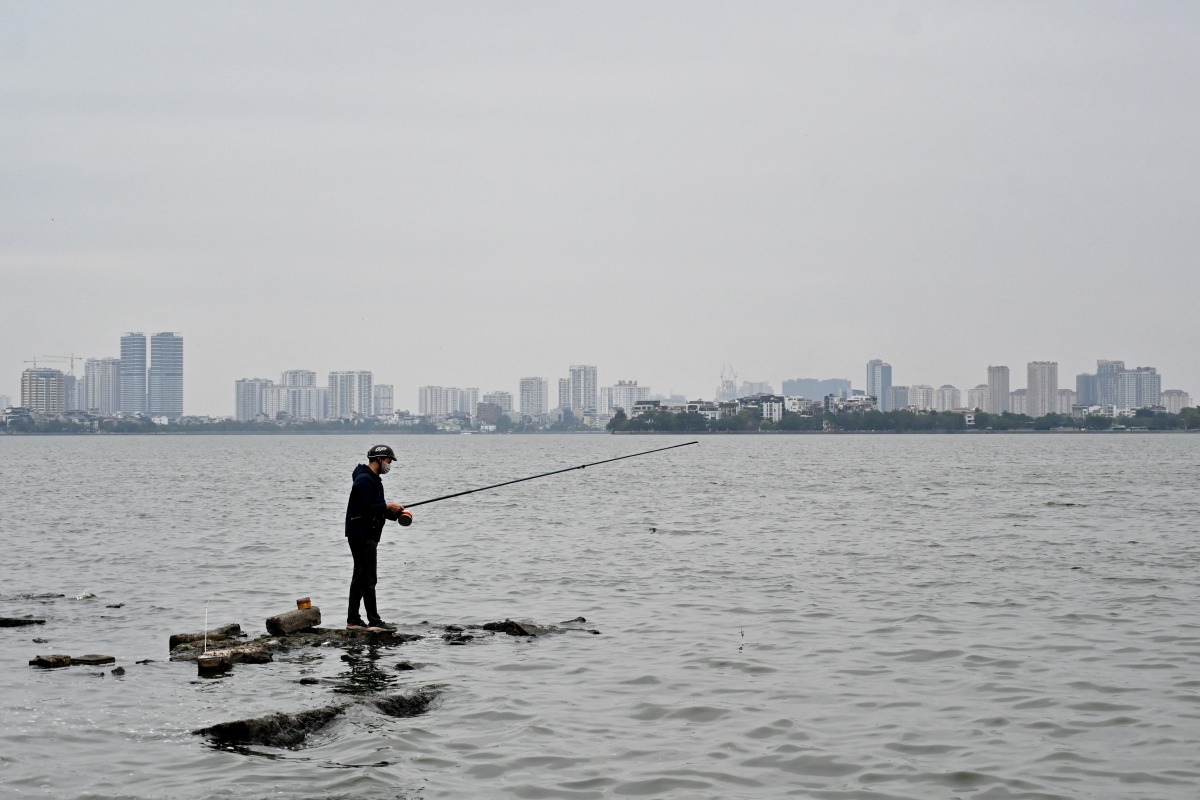 A man stands on rocks as he fishes in West Lake in Hanoi on November 27, 2024. Photo by Nhac NGUYEN / AFP