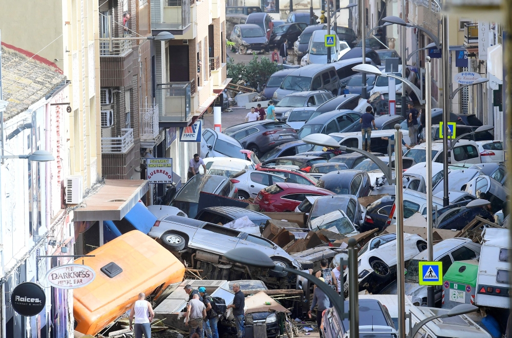 File: Pedestrians stand next to piled up cars following deadly floods in Sedavi, south of Valencia, eastern Spain, on October 30, 2024. (Photo by Jose Jordan / AFP)