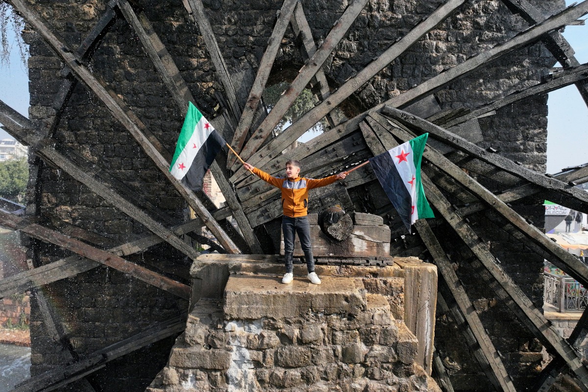 Photo used for representation purposes. A boy waves the opposition Syrian flag as he stands in one of the water wheels, or norias, in Hama, after anti government fighters captured of the central city, on December 6, 2024. Photo by Omar HAJ KADOUR / AFP.