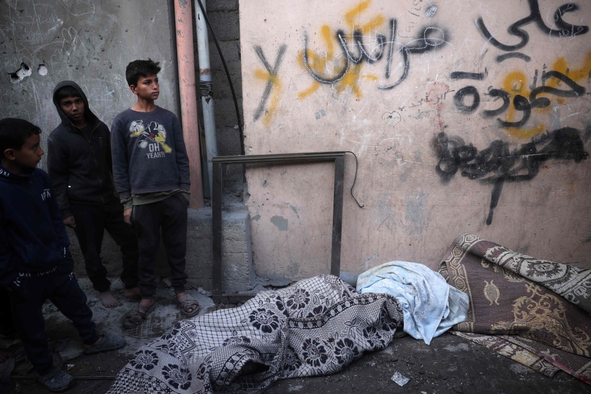 Palestinians stand next to covered bodies, recovered from the rubble of a building after an Israeli strike, on the Nuseirat refugee Camp in the central Gaza Strip on December 7, 2024. (Photo by Eyad BABA / AFP)
