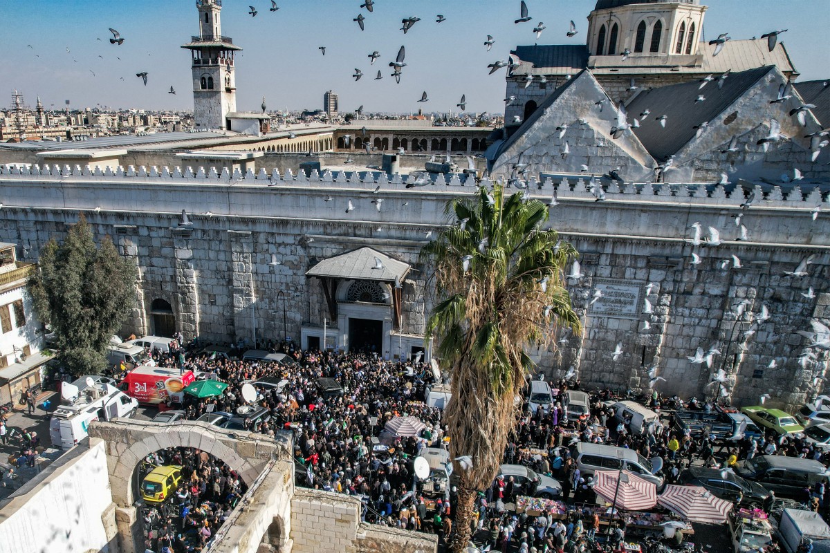 This aerial view shows pigeons flying as people crowd outside the 8th-century Umayyad mosque and the Hamidiyah covered market in the old city of Damascus on December 13, 2024 during first weekly Muslim Friday prayers since the ouster of president Bashar al-Assad. Photo by Bakr ALKASEM / AFP.