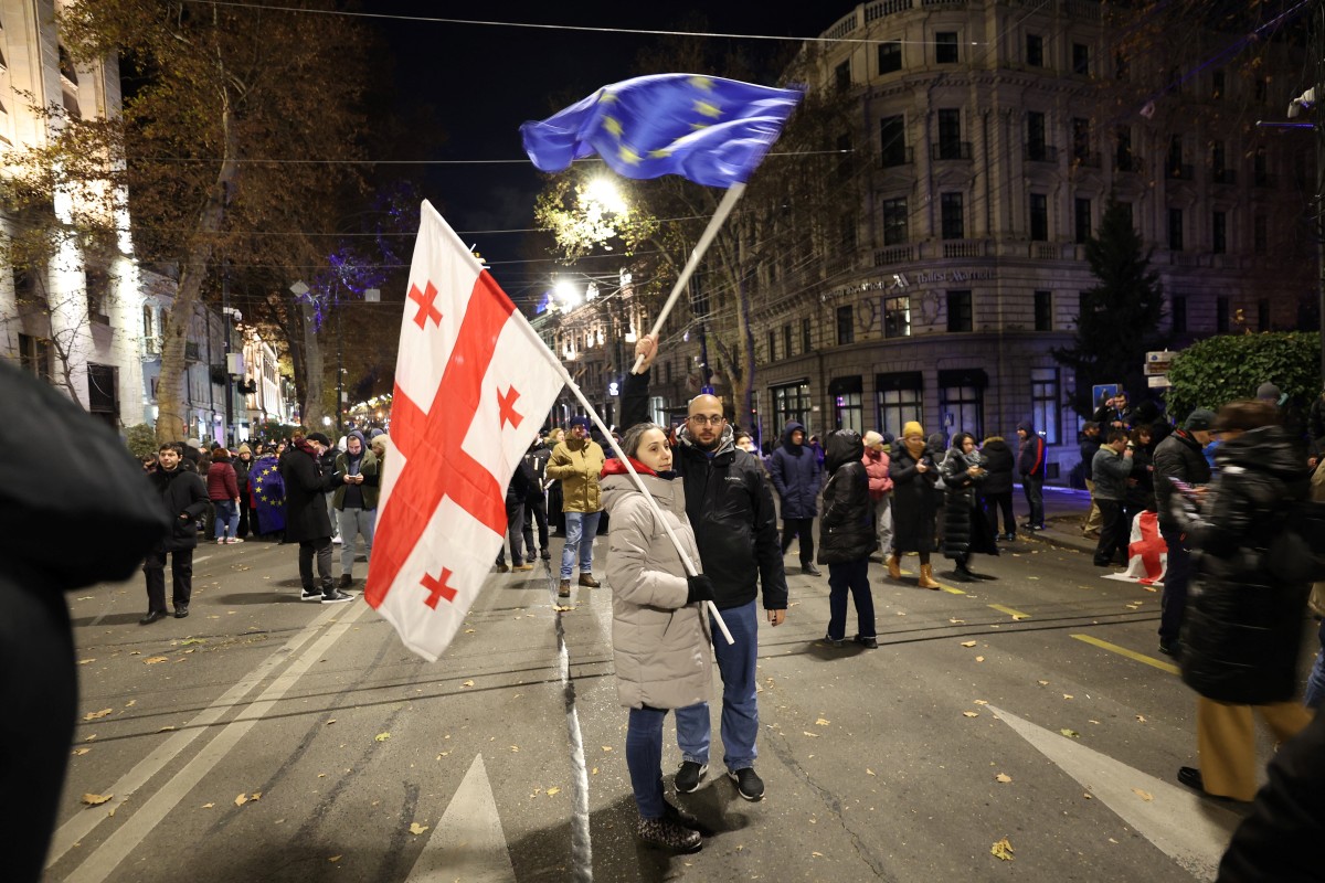 Anti-government protesters wave a Georgian (L) and European Union (R) flag during a demonstration against the Georgian government's postponement of European Union accession talks until 2028, outside the Parliament in central Tbilisi on December 12, 2024. Photo by Giorgi ARJEVANIDZE / AFP.