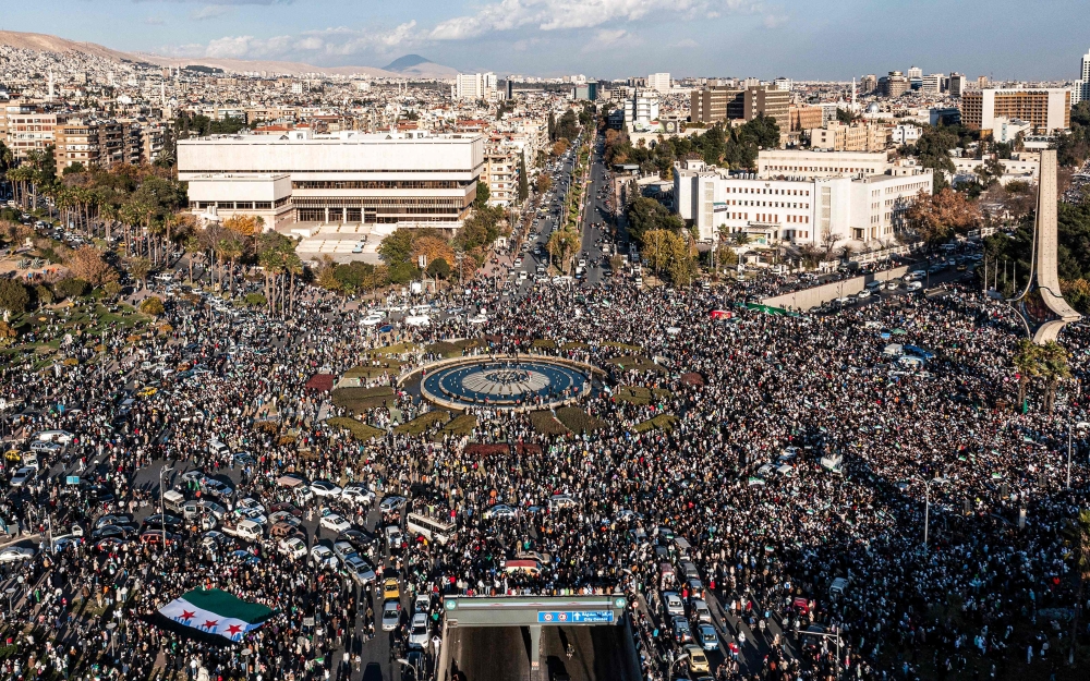 This aerial view shows people celebrating the ouster of Syria's president Bashar Al Assad near the landmark Damascus Sword sculpture at the Umayyad Square in central Damascus on December 13, 2024. (Photo by Sameer Al-Doumy / AFP)