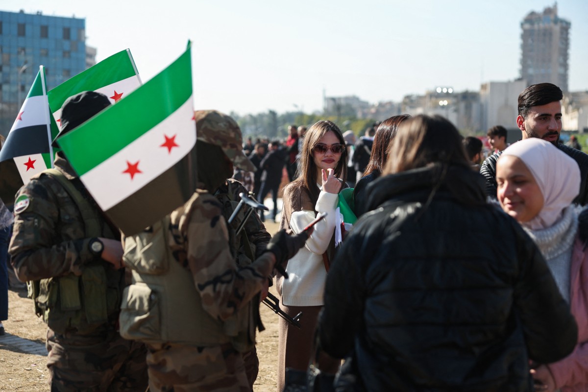 Rebel fighters stand near protesters during a student rally near the campus of the Damascus University in the Syrian capital on December 15, 2024. Photo by Omar HAJ KADOUR / AFP.