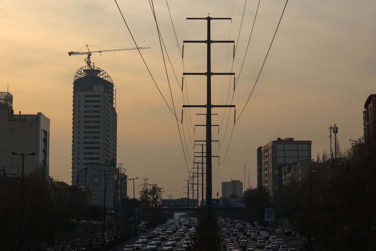 Traffic flows on a main road past electricity transmission towers in Tehran on December 16, 2024. Iran has suspended operations at several power plants over fuel shortages that have been intensified by rising demand during a spell of freezing weather. (Photo by ATTA KENARE / AFP)
