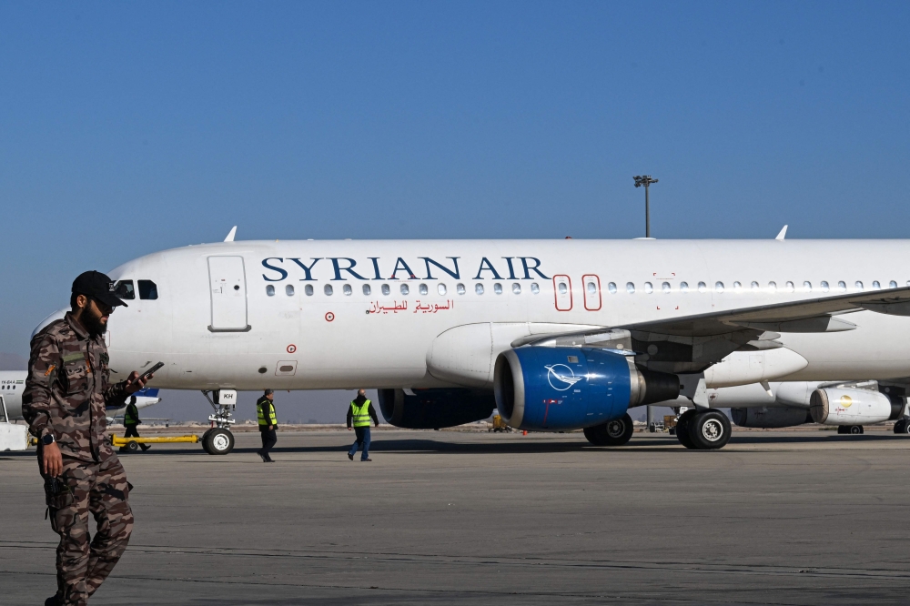 A fighter walks past as ground personnel prepare a Syrian Air aircraft for departure to the city of Aleppo, at the Damascus international airport on December 18, 2024. (Photo by Louai Beshara / AFP)