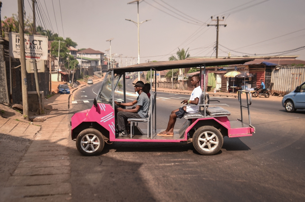 Self-thought innovator James Samba (L) drives an eco-friendly electric vehicle he made from scrap metals in Freetown on December 18, 2024. (Photo by Saidu Bah / AFP)