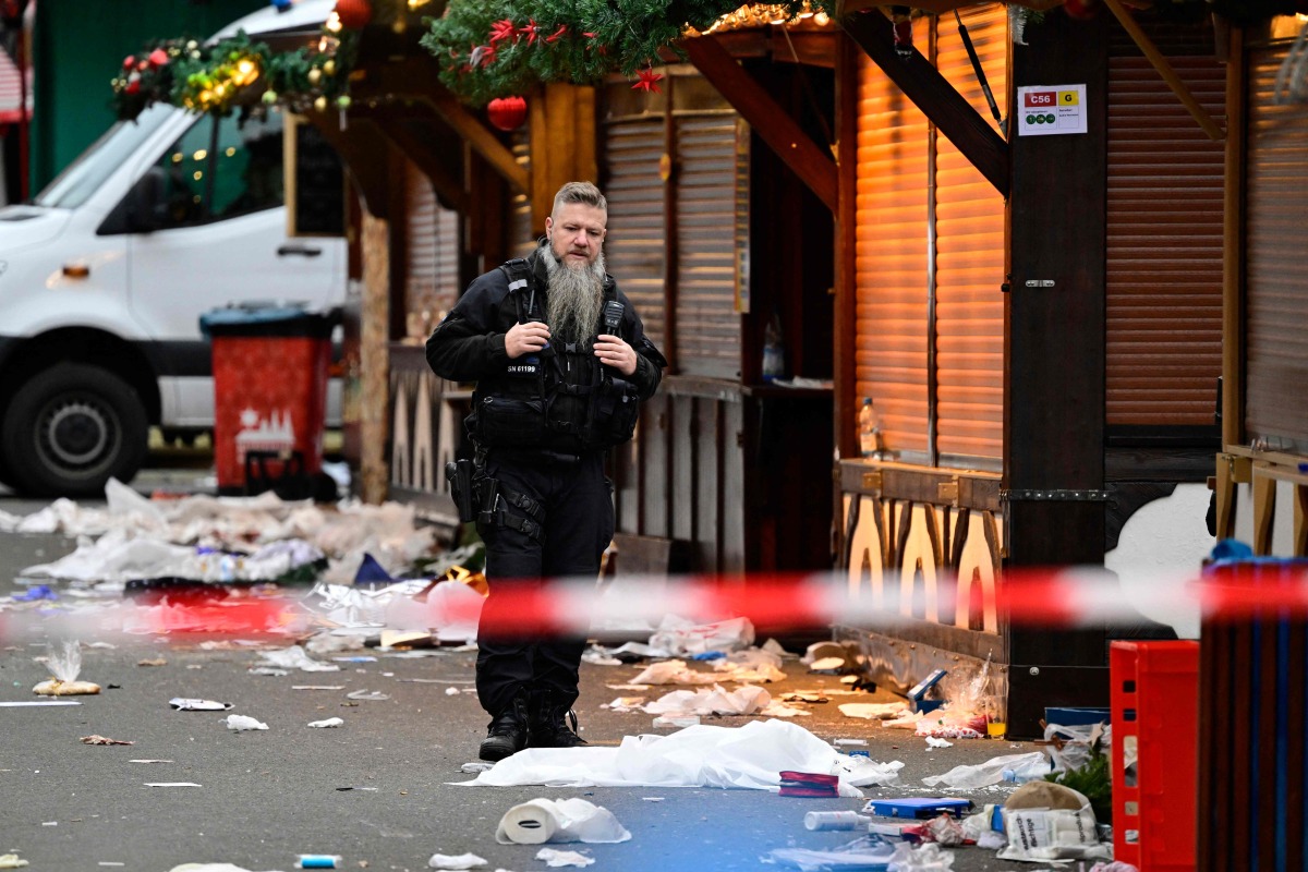 Debris a closed stalls are seen as a police officers stands on the site of a car-ramming attack on a Christmas market in Magdeburg, eastern Germany, on December 21, 2024. (Photo by John MACDOUGALL / AFP)