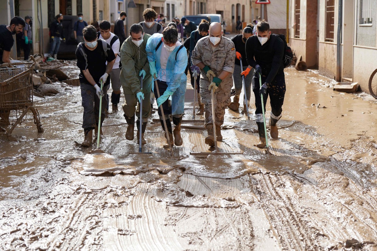 File: People with masks and soldier remove mud in a flooded street on November 6, 2024, in Catarroja, in the region of Valencia, eastern Spain, in the aftermath of deadly floods. (Photo by Cesar Manso / AFP)