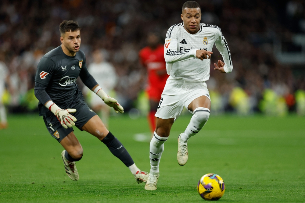 Real Madrid's French forward #09 Kylian Mbappe and Sevilla's Spanish goalkeeper #01 Alvaro Fernandez (left) vie for the ball during the Spanish league football match between Real Madrid CF and Sevilla FC at the Santiago Bernabeu stadium in Madrid on December 22, 2024. (Photo by Oscar Del Pozo / AFP)