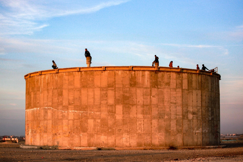 Children sit at sunset atop a concrete water storage tank overlooking the Hamad Residential City complex in the north of Khan Yunis in the southern Gaza Strip on December 22, 2024. (Photo by Bashar Taleb / AFP)