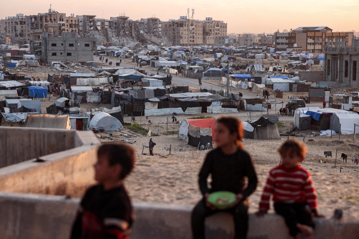 Children sit together overlooking a view of tents sheltering Palestinians displaced by confict by the Hamad Residential City complex in the north of Khan Yunis in the southern Gaza Strip on December 22, 2024. Photo by BASHAR TALEB / AFP