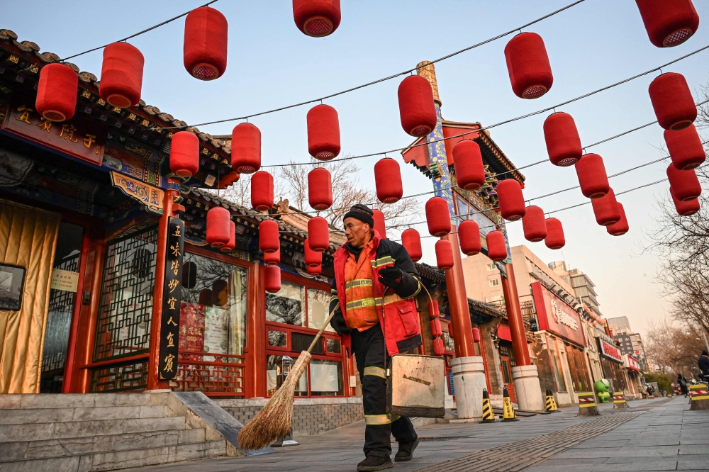 A cleaner carrying a broom and a trash bin walks along a street in Beijing on December 24, 2024. (Photo by Jade Gao / AFP)