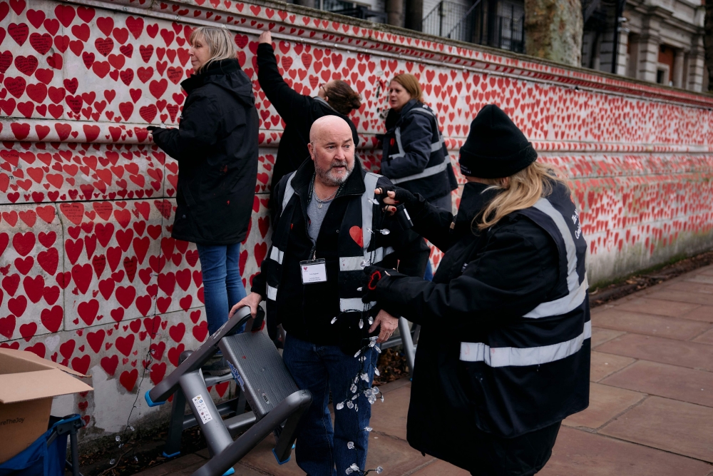 Volunteers hang lights on The National Covid Memorial Wall, dedicated to those who lost their lives to Covid-19, on the bank of the River Thames in London on December 20, 2024. (Photo by Benjamin Cremel / AFP)