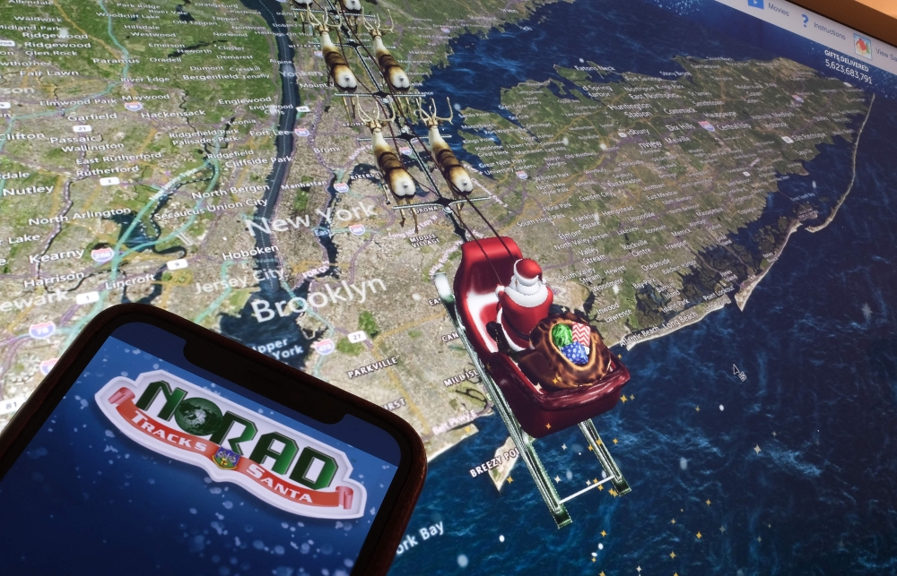 (Files) This illustration photo shows the NORAD logo on a cell phone screen while the tracker follows Santa flying over New York City on a computer monitor in Los Angeles on December 24, 2023. (Photo by Chris Delmas / AFP)