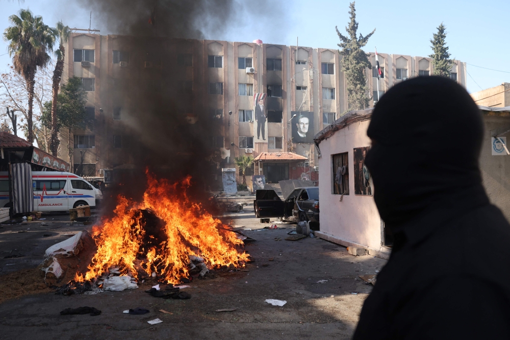 A man watches a pile of illicit drugs burn, as Syria's new authorities burn drugs reportedly seized from a security branch, in Damascus on December 25, 2024. (Photo by Omar Haj Kadour / AFP)