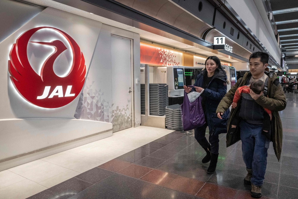 People walk past a check-in counter for Japan Airlines at the departures hall of Haneda Airport in Tokyo on December 26, 2024. (Photo by Yuichi YAMAZAKI / AFP)