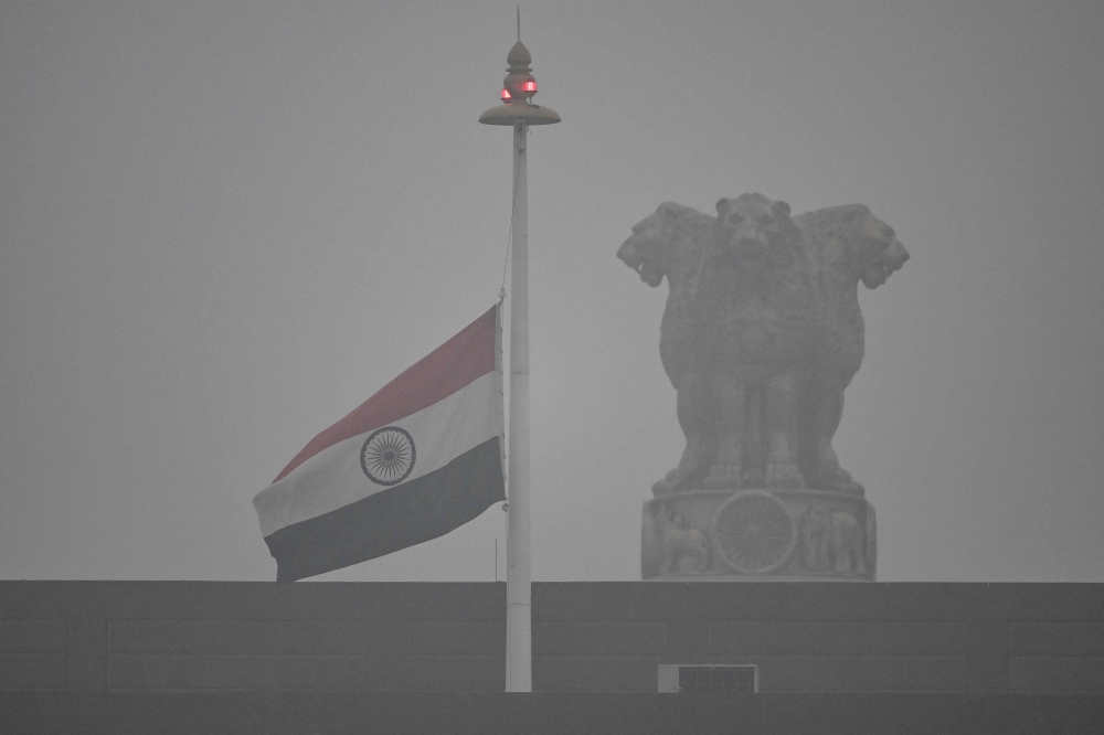 The Indian national flag flies half-mast at the Parliament to mourn the death of former Indian Prime Minister Manmohan Singh, as it rains in New Delhi on December 27, 2024. (Photo by Arun Sankar / AFP)