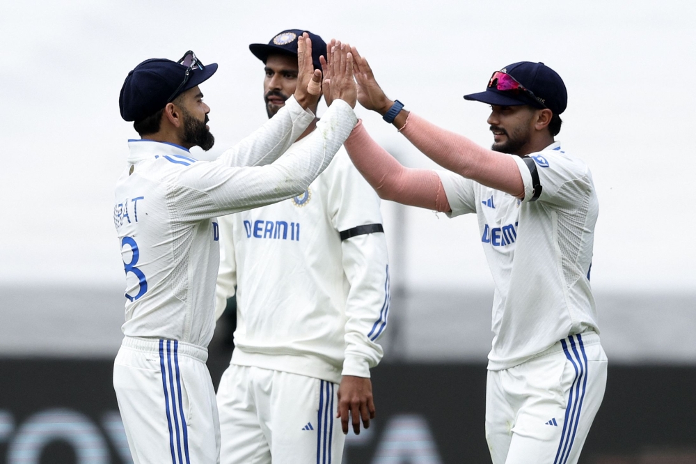 India's Virat Kohli (L) and Nitish Kumar Reddy (R) celebrate the wicket of Australia's Pat Cummins on the second day of the fourth cricket Test match between Australia and India at the Melbourne Cricket Ground (MCG) in Melbourne on December 27, 2024. (Photo by Martin Keep / AFP) 